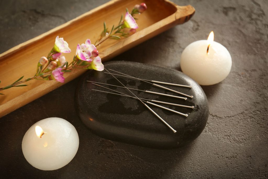 Acupuncture needles with stone and candles on textured background